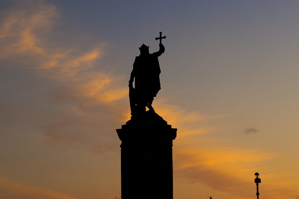 Dramatic silhouette of a historic statue in Gijón, Spain against a vibrant sunset sky.